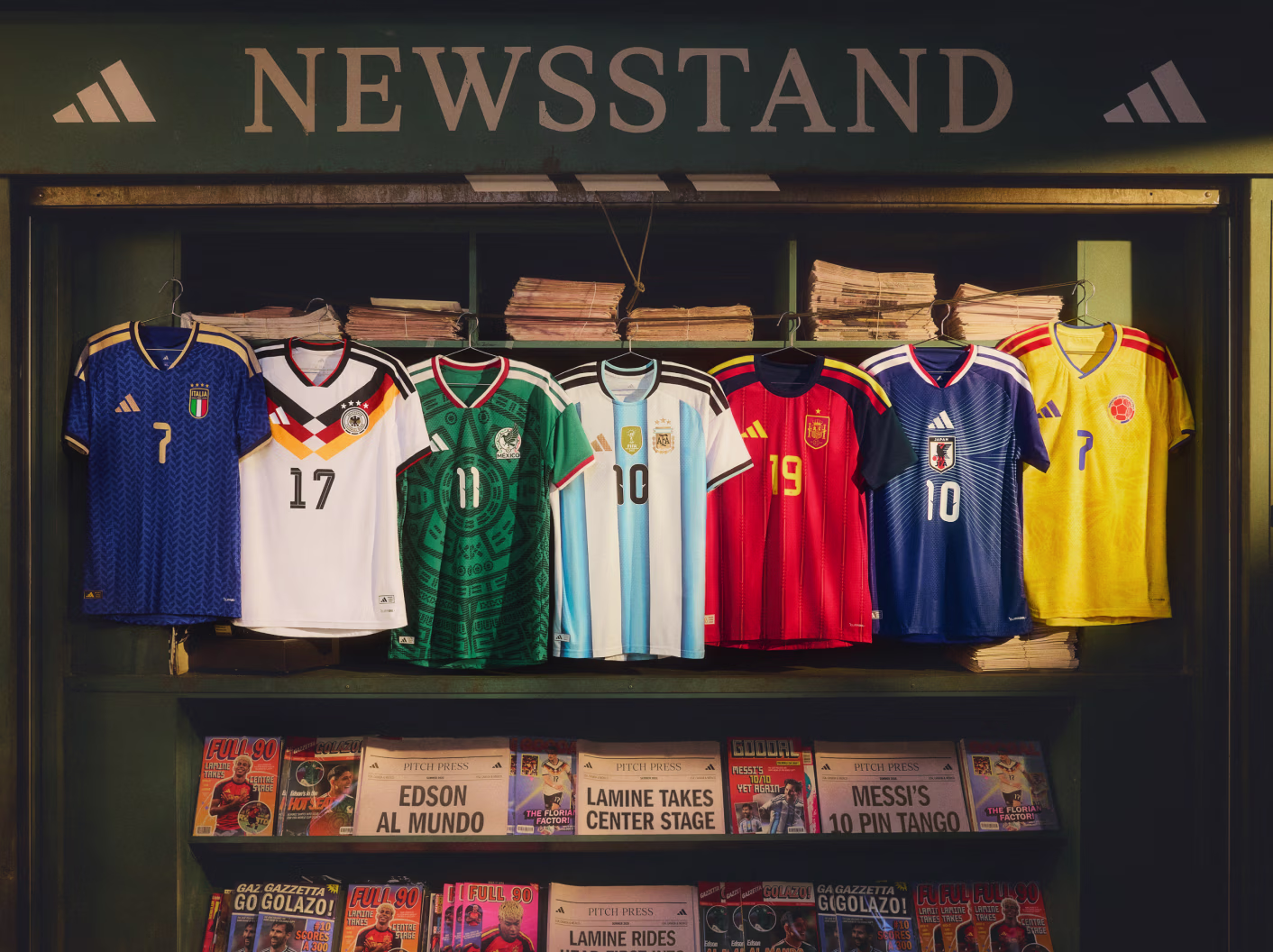 Newsstand display of seven soccer jerseys from Italy, Germany, Mexico, Argentina, Spain, Japan, and Colombia.