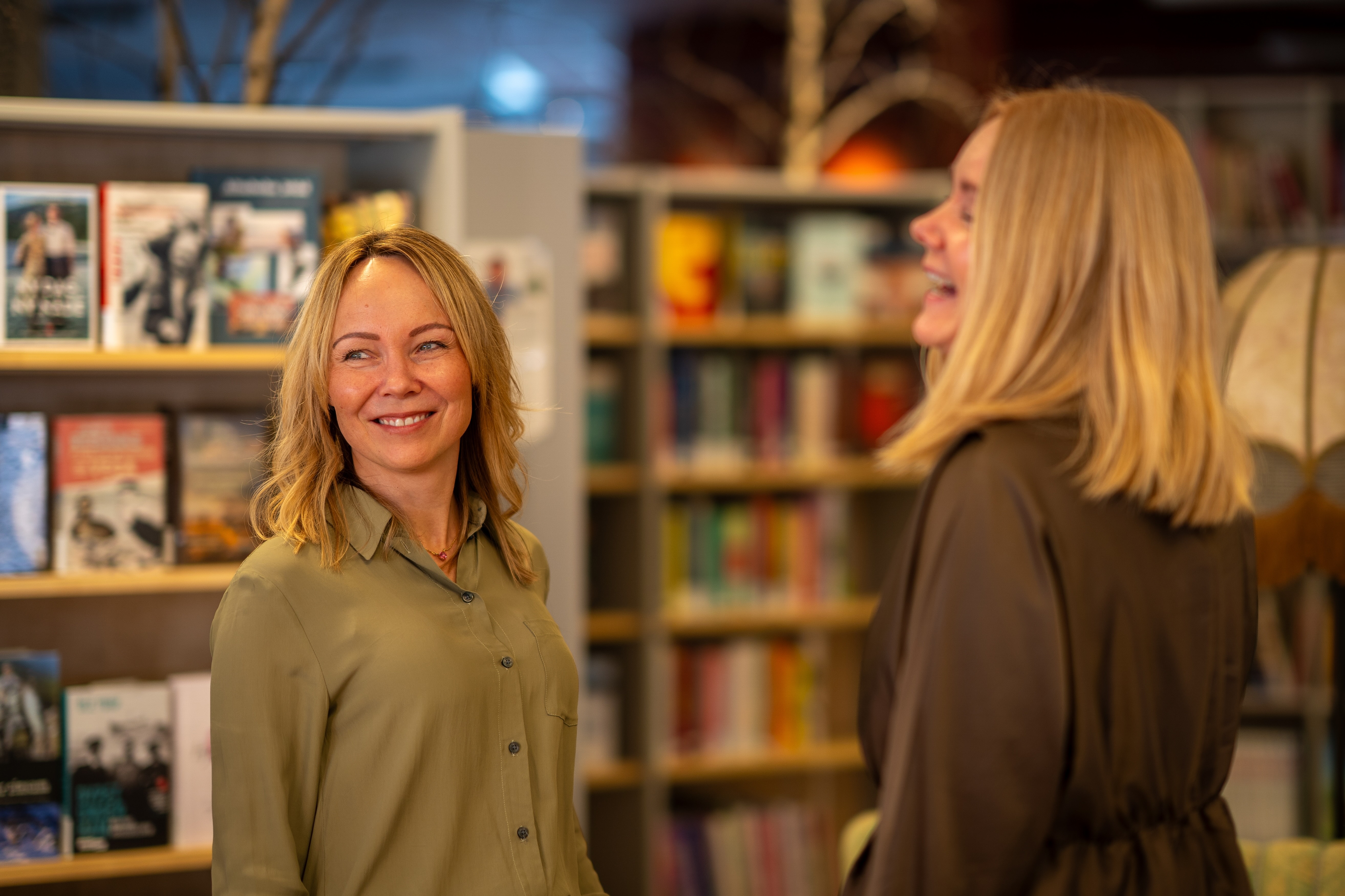 Lone Hegg og Mette Suhr Berg ler og smiler sammen på biblioteket i Alta.