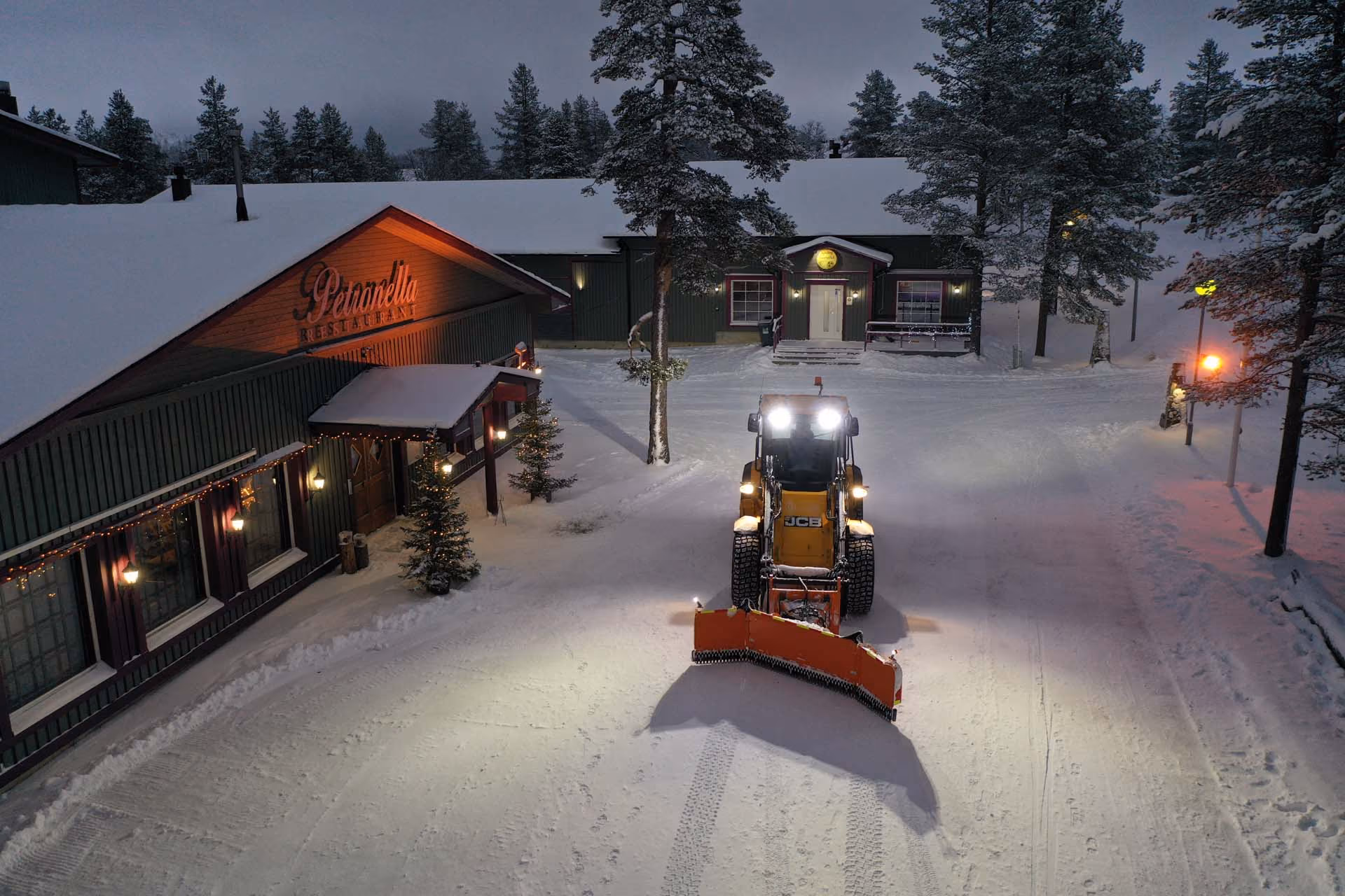 En hjullaster med plog foran en snødekt restaurant om kvelden.