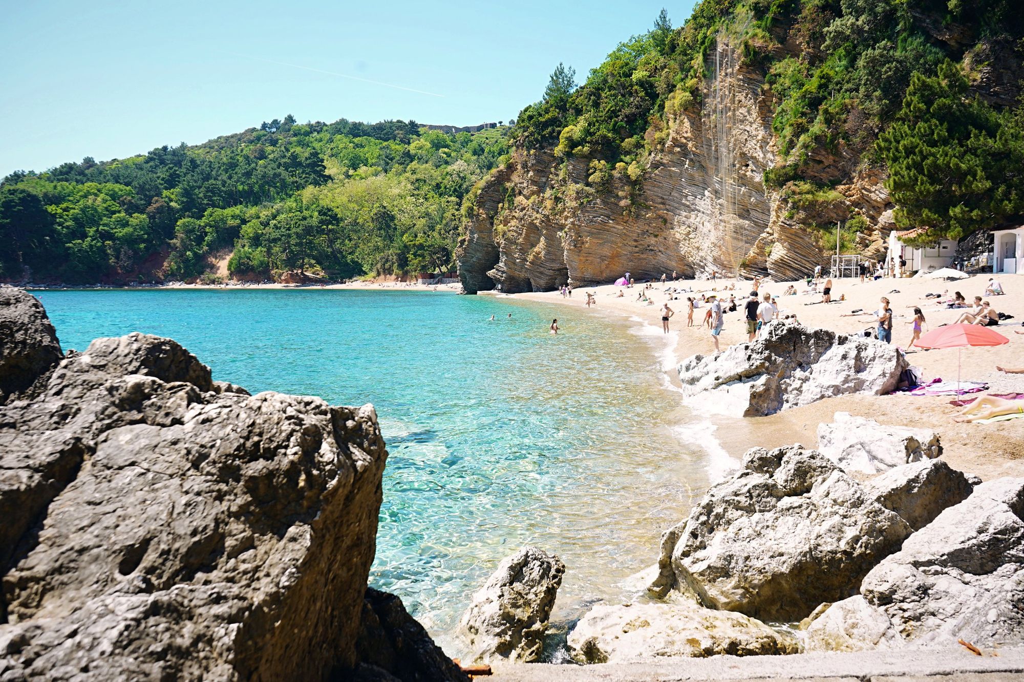 Clear turquoise water, rocks and a cliff-backed beach on the coast of Montenegro