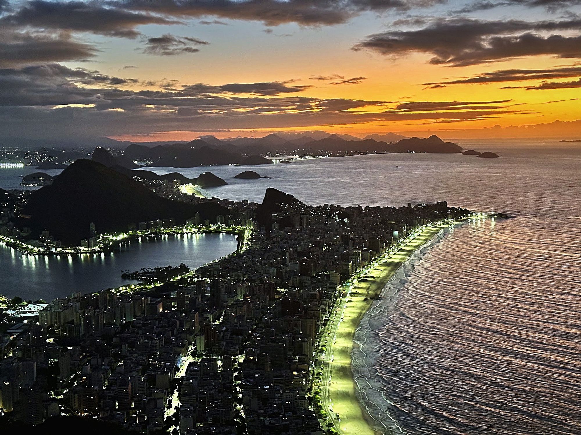 Rio de Janeiro from above at dusk, the beach lit along the bay