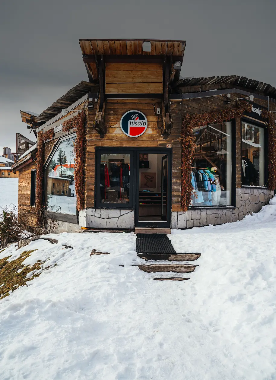 Boutique Fusalp en bois avec affichage de vêtements, entourée de neige et ciel gris.