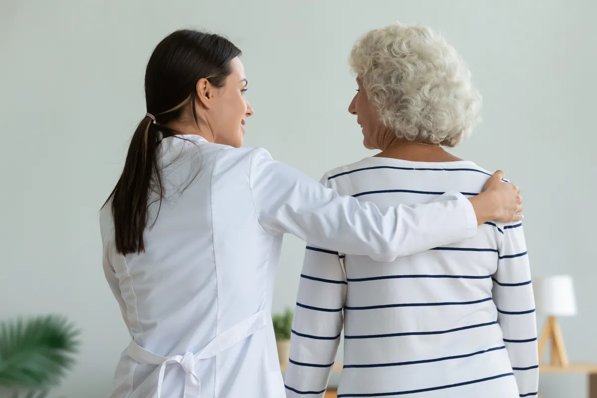 Doctor with arm around senior woman walking together.