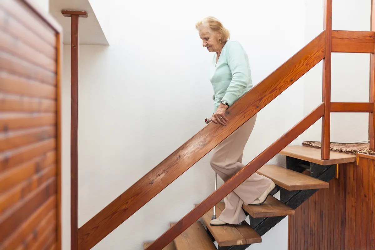 Elderly woman carefully walking down stairs holding railing.