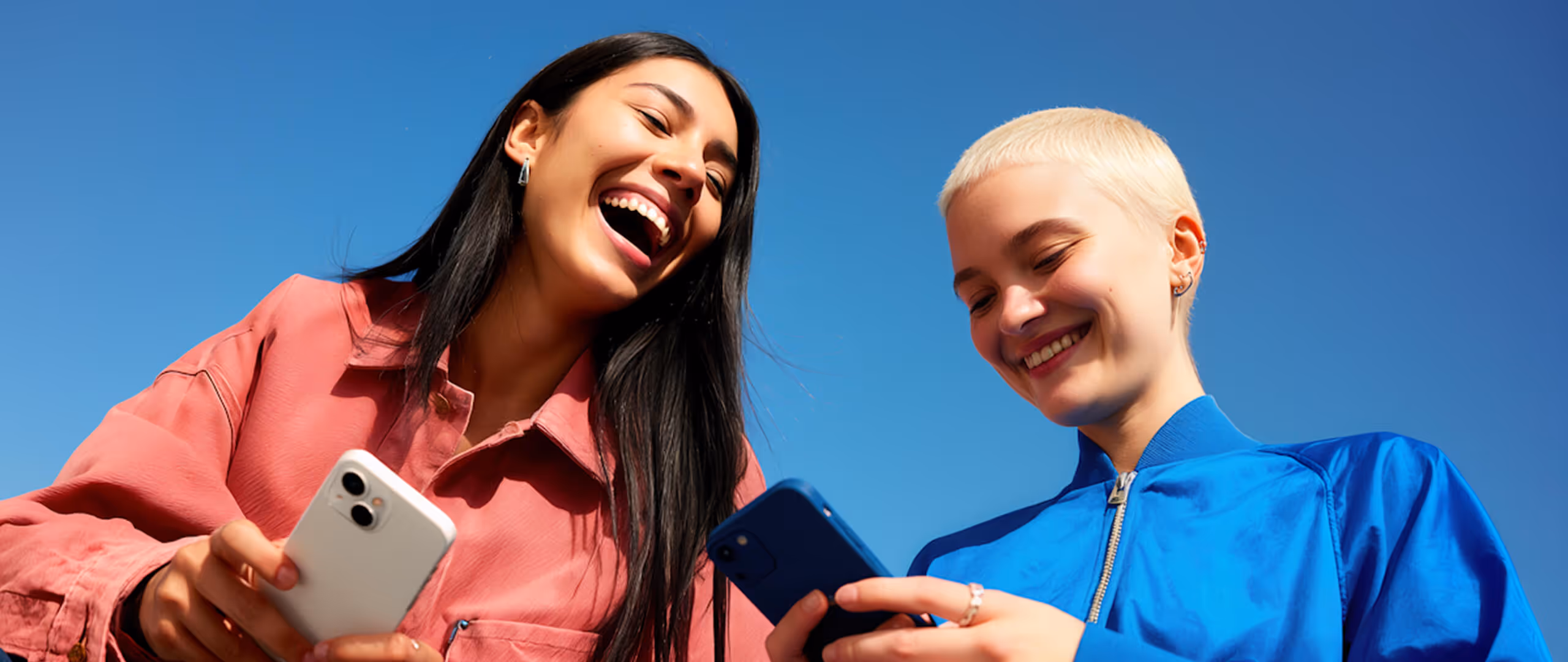 Woman in a gray blazer sitting on a beige couch using a laptop, with a coffee cup and tablet on a wooden table nearby.