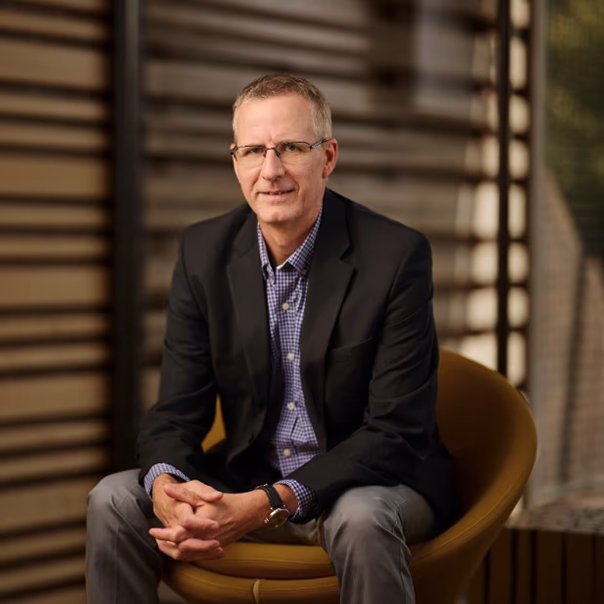 Portrait of a young man with blue eyes and short blonde hair wearing a blue suit jacket and white shirt against a dark background.
