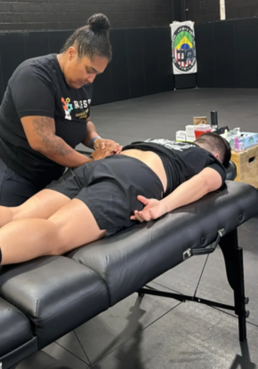 A person receiving a back massage while lying face down on a massage table in a gym setting.