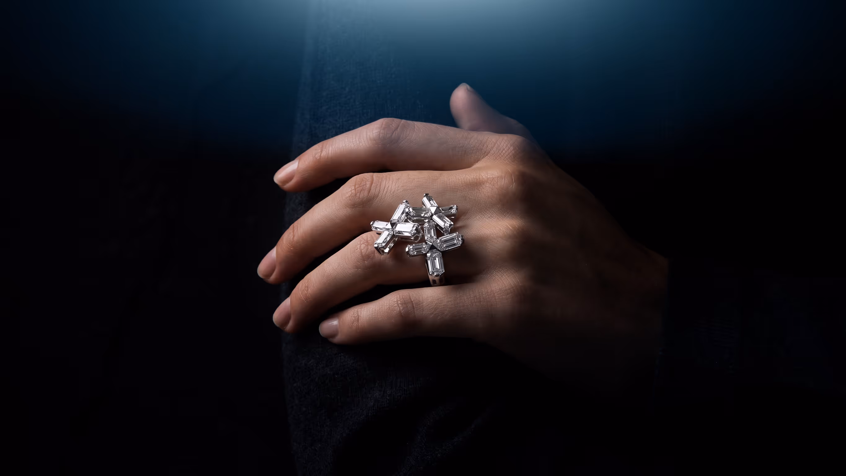 Hand wearing a silver ring with multiple rectangular clear gemstones on a dark background.