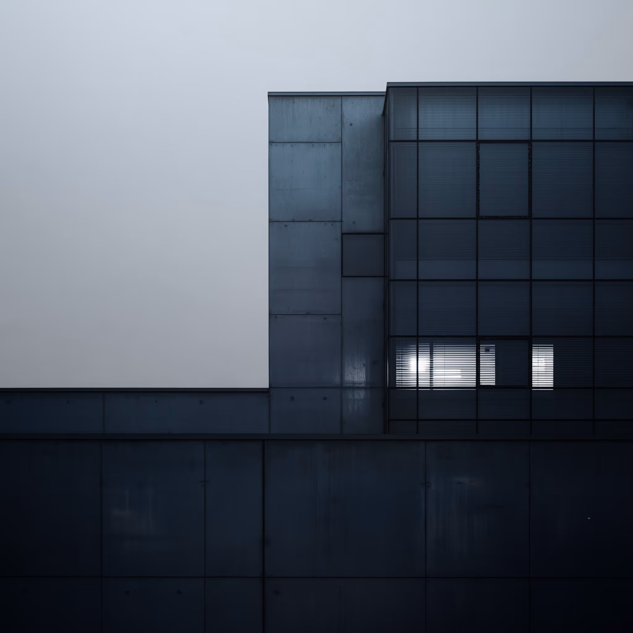Modern dark blue concrete building with glass windows and blinds partially open, some light inside.