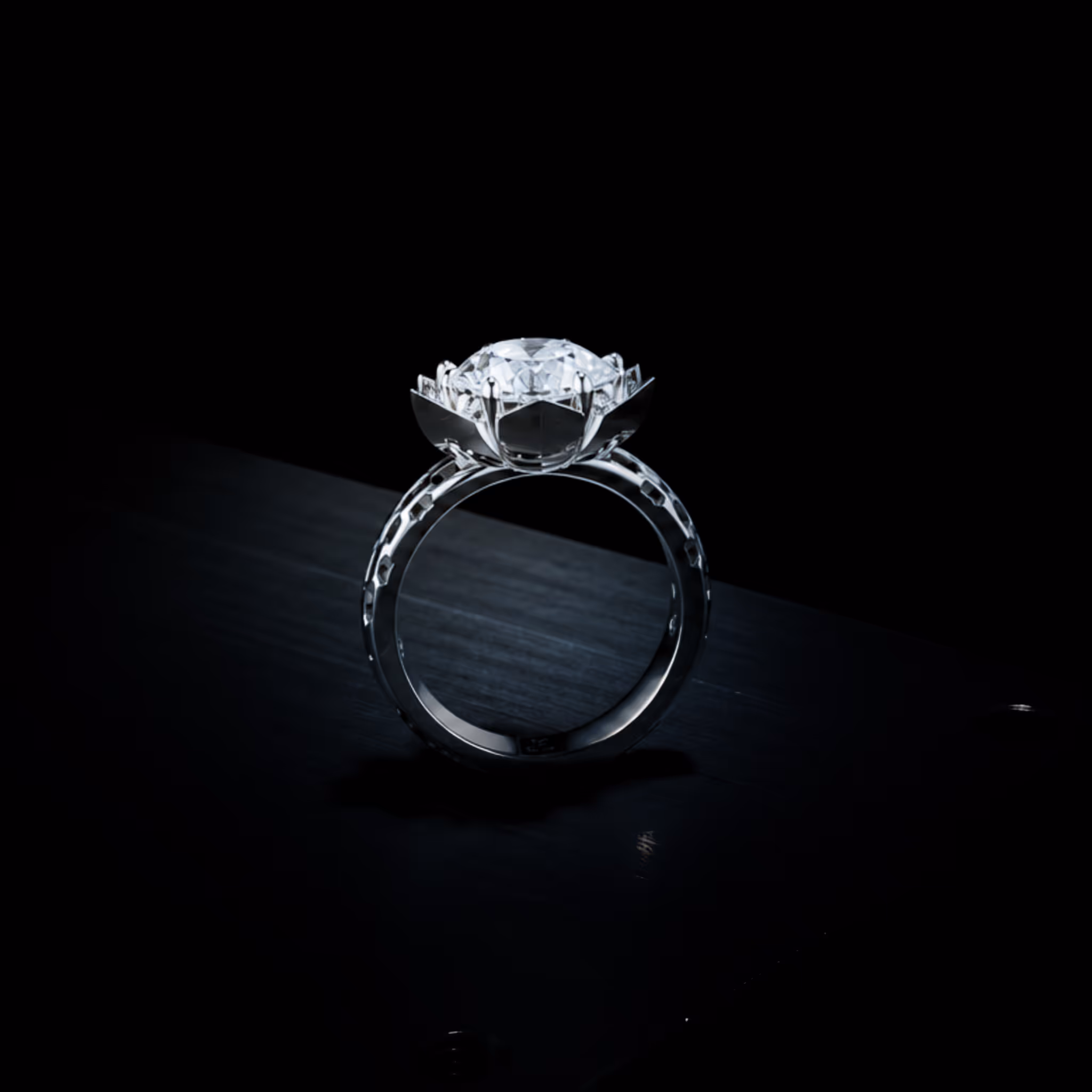 Close-up of a silver ring with a large, round diamond set in a flower-shaped mount on a dark background.