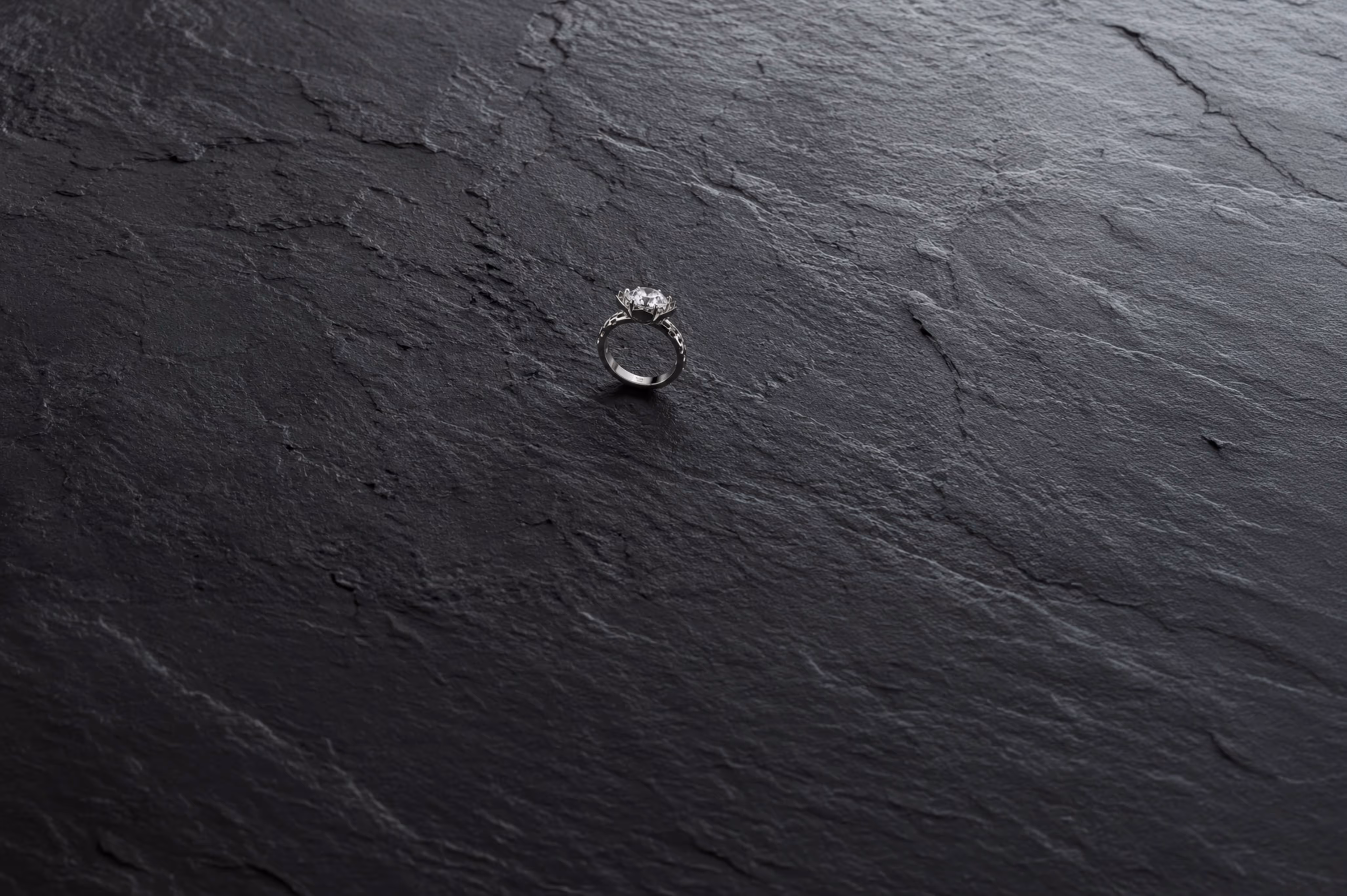 Silver engagement ring with diamond on textured dark stone surface.
