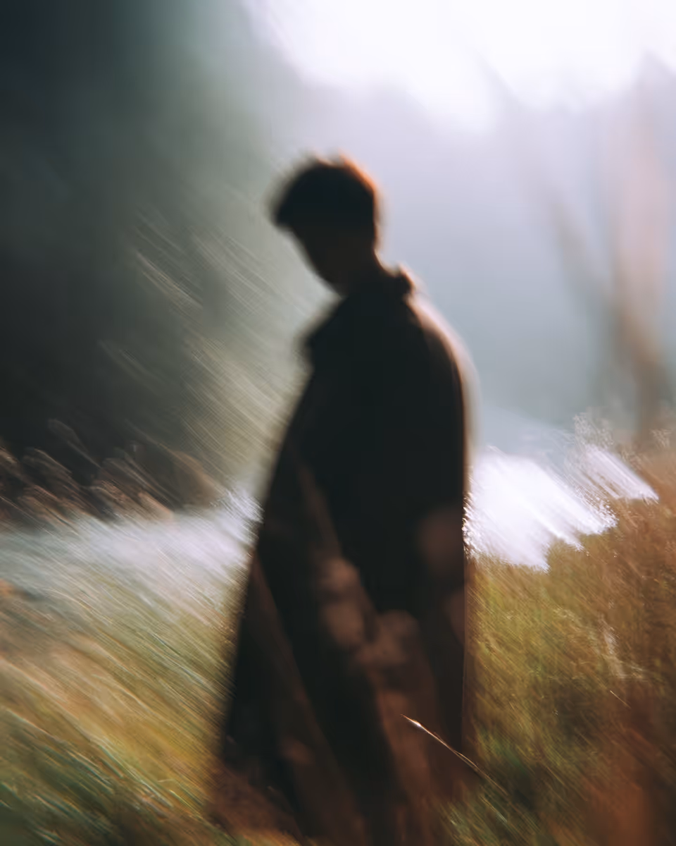 Silhouette floue d'une personne debout à l'extérieur dans un environnement naturel lumineux.