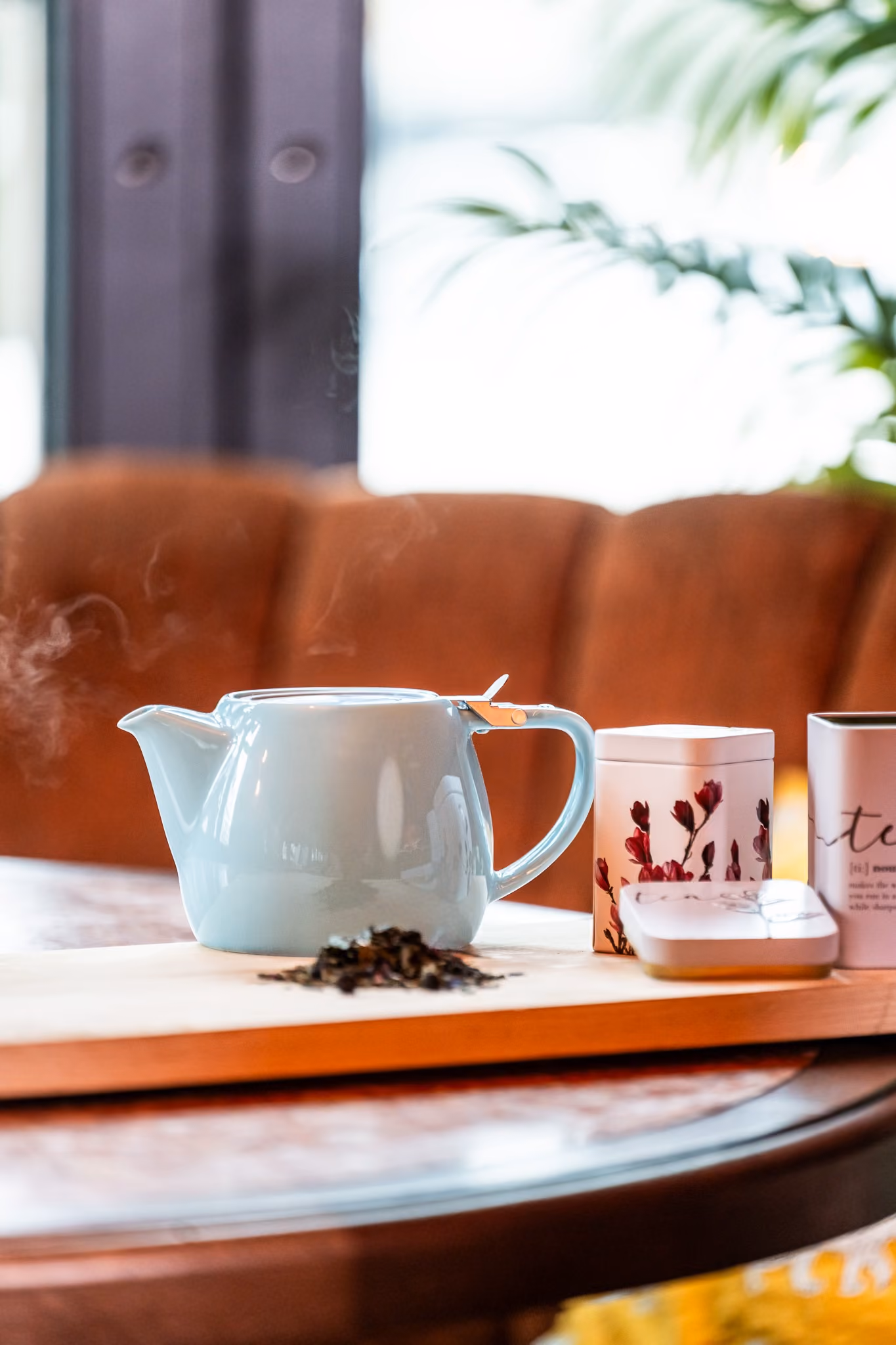 Stilleven met een witte theepot, losse thee en decoratieve theeblikken op een houten plank.