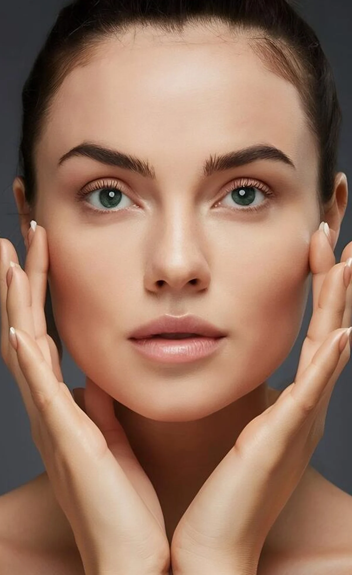 Close-up of a woman with clear skin touching her face gently with both hands.