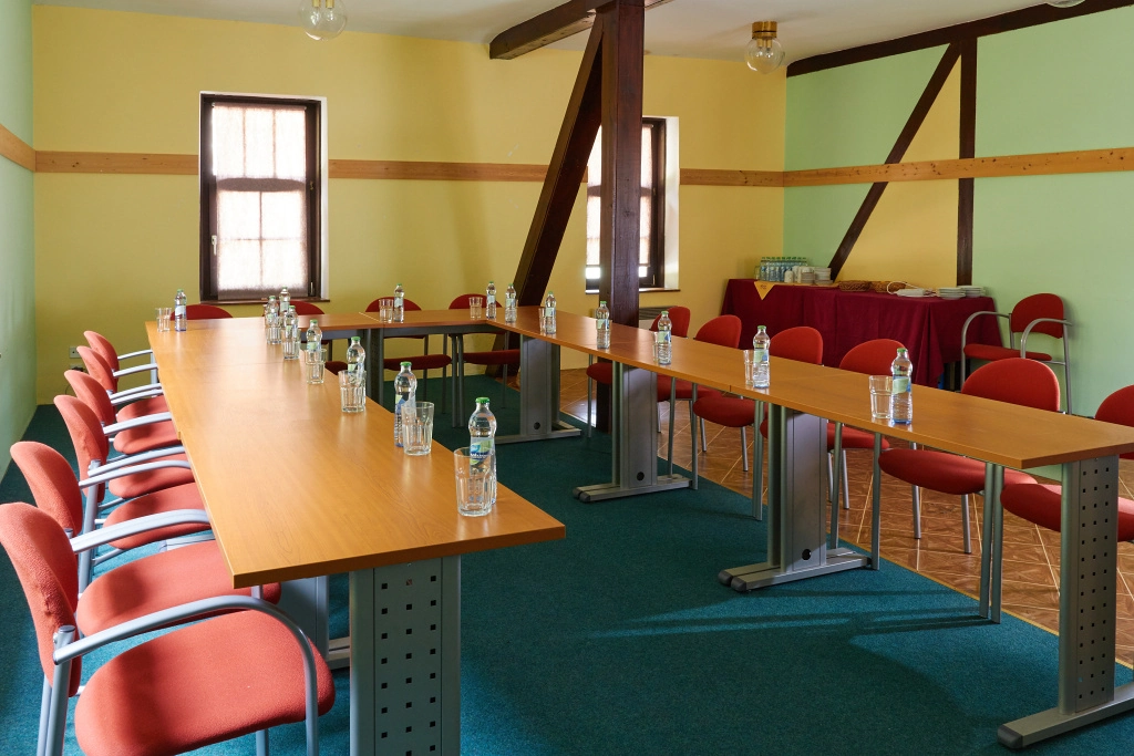Konferenční místnost s uspořádáním U, židle s oranžovým čalouněním a stolem s lahvemi vody a sklenicemi.