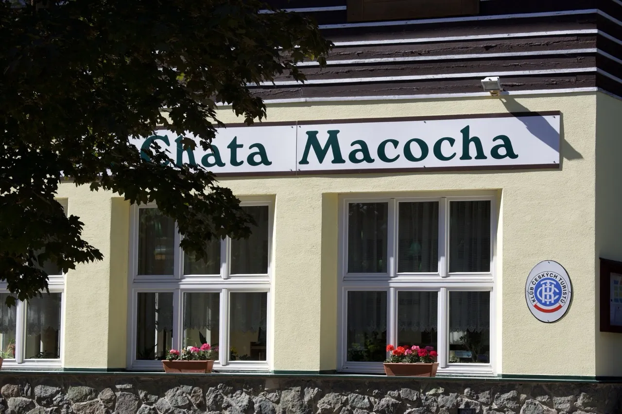 Budova s nápisem Chata Macocha, květiny ve truhlících pod okny a znak Klubu českých turistů.
