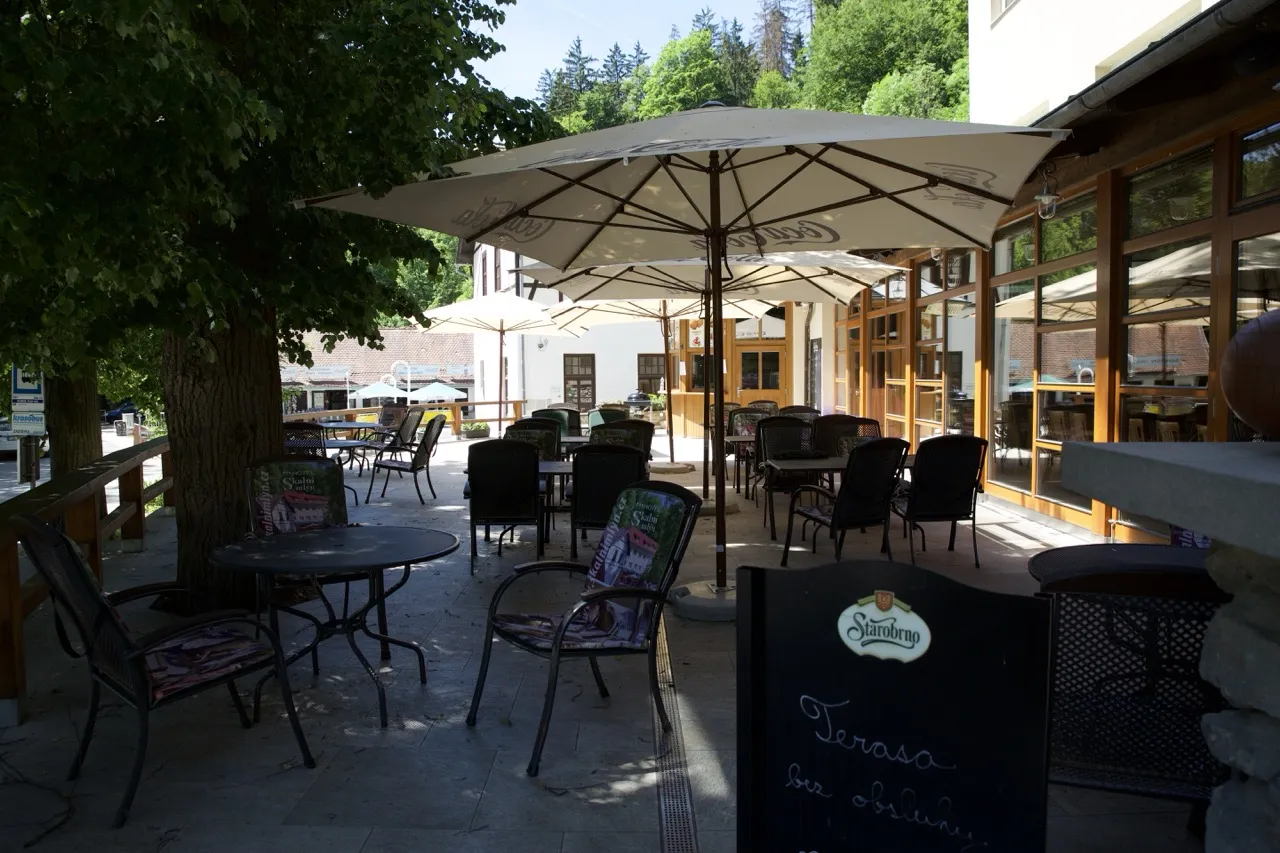 Venkovní terasa s kovovými stolem, židlemi a velkými bílými slunečníky v restauraci.