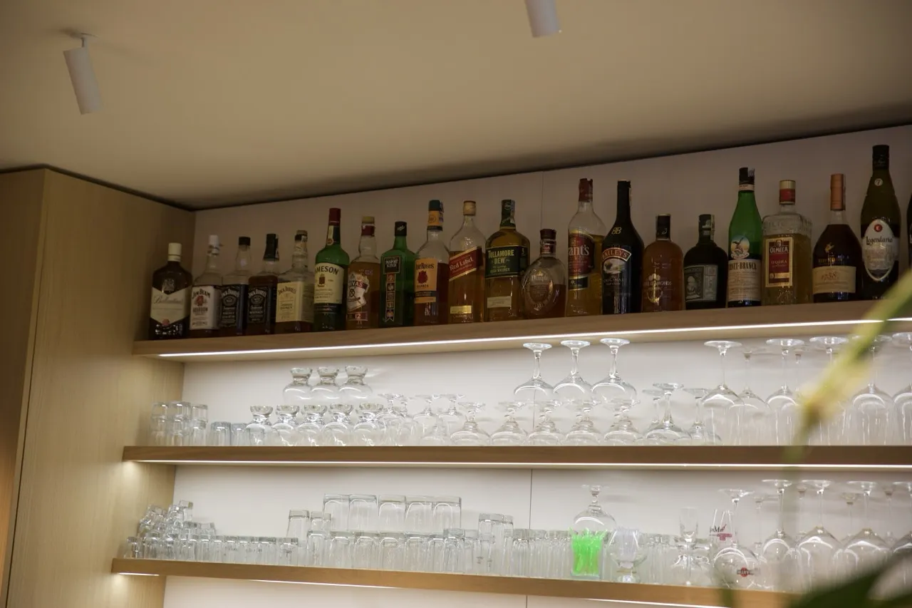Policejní police s různými lahvemi alkoholu nahoře a několika řadami prázdných sklenic pod nimi.