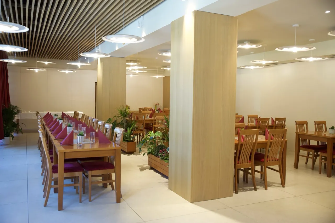Modern dining room with wooden tables and chairs, red napkins, and hanging ceiling lights.