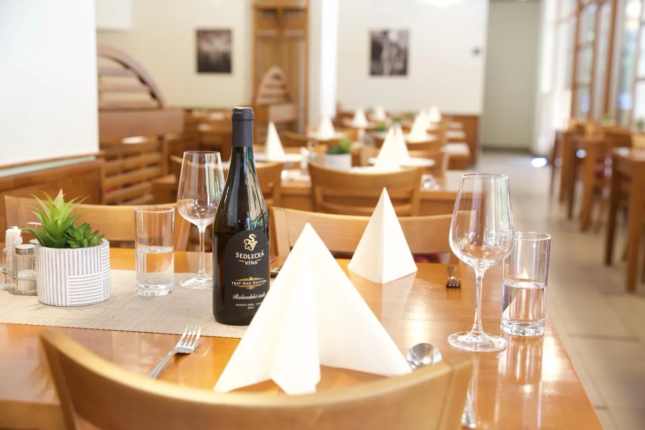 Restaurace s dřevěným nábytkem, stolem se sklenicí, vínem a bílými složenými ubrousky.