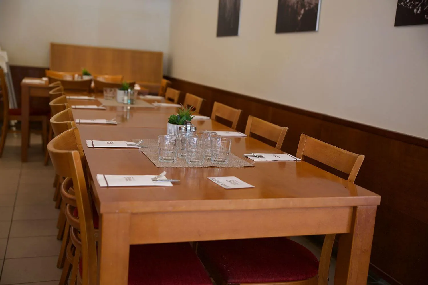 Dlouhý dřevěný stůl s nastavenými sklenicemi, příbory a jídelními lístky v restauraci.