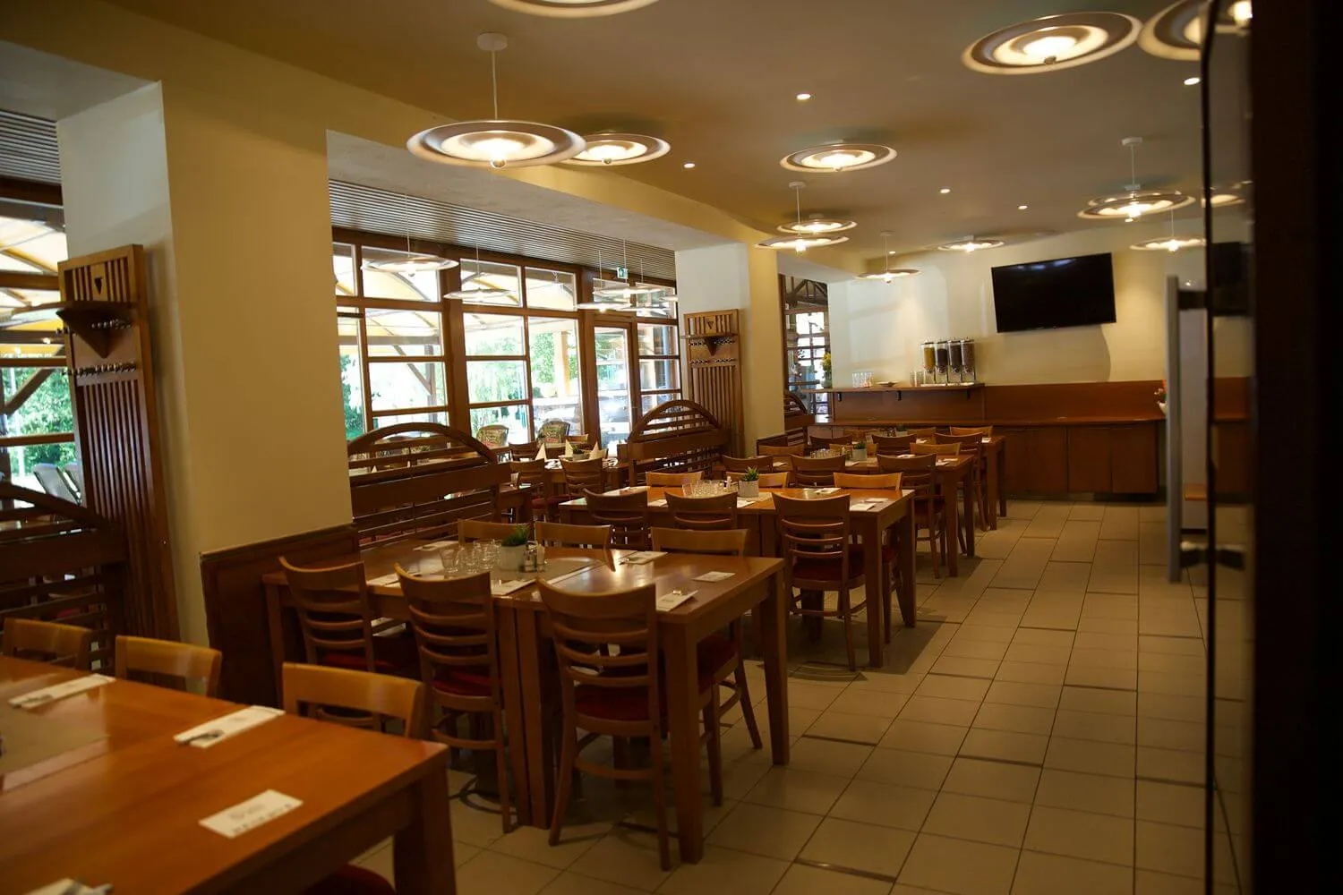 Pohled do moderní restaurace s dřevěným nábytkem a stoly připravenými na hosty.