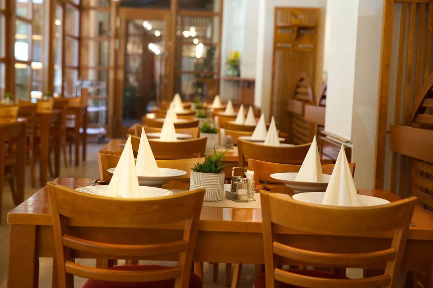 Restaurace s dřevěným nábytkem, na stolech talíře s papírovými ubrousky ve tvaru kužele.