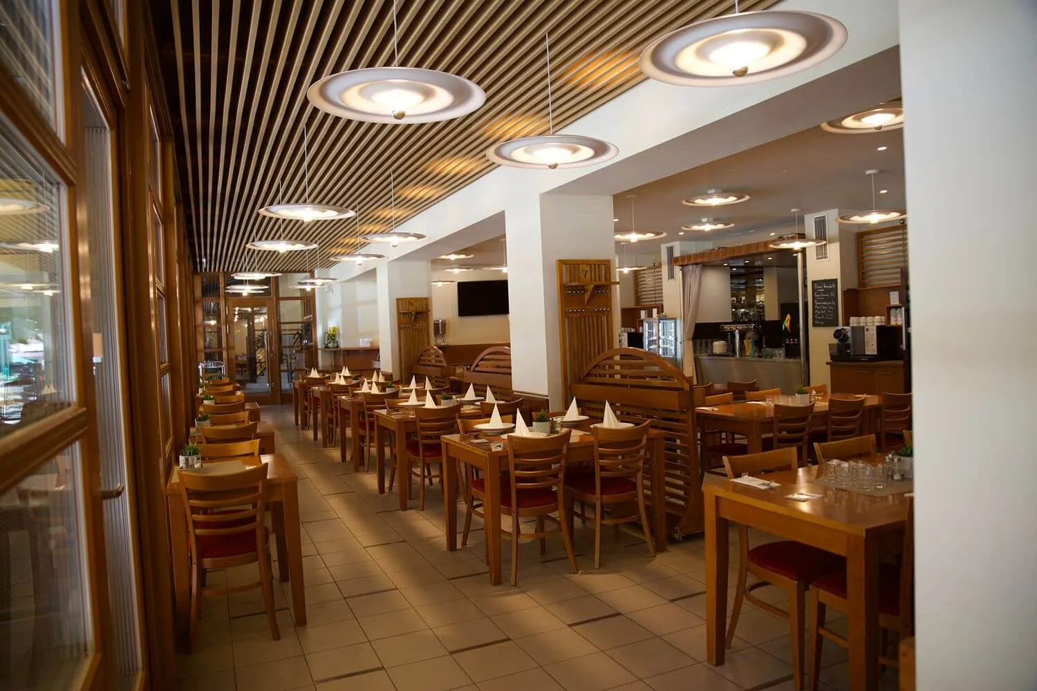 Interiér restaurace s dřevěnými stolky a židlemi, ubrusy a moderním osvětlením.