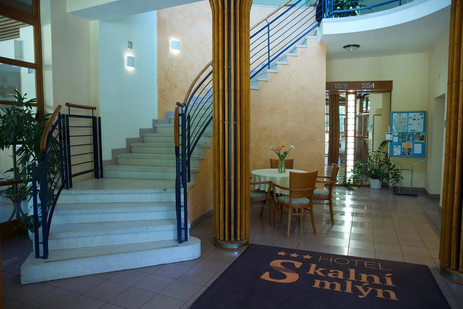 Interiér hotelu se schodištěm, stolkem s květinou a kobercem s nápisem Hotel Skalní mlýn.