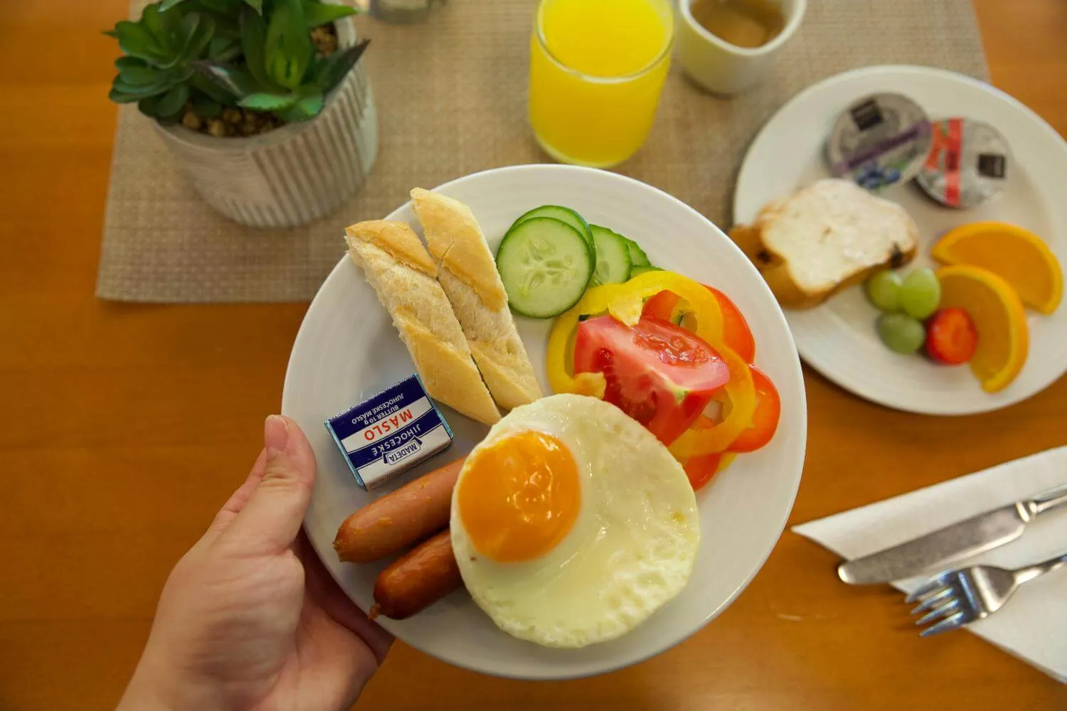 Talíř se snídaní: volské oko, párky, bageta, zelenina, máslo a sklenice džusu.