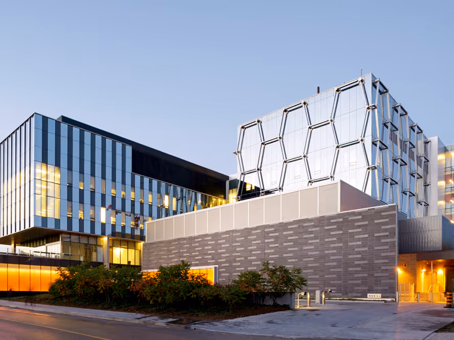 Modern multi-story building with glass windows and honeycomb-patterned reflective panels at dusk.