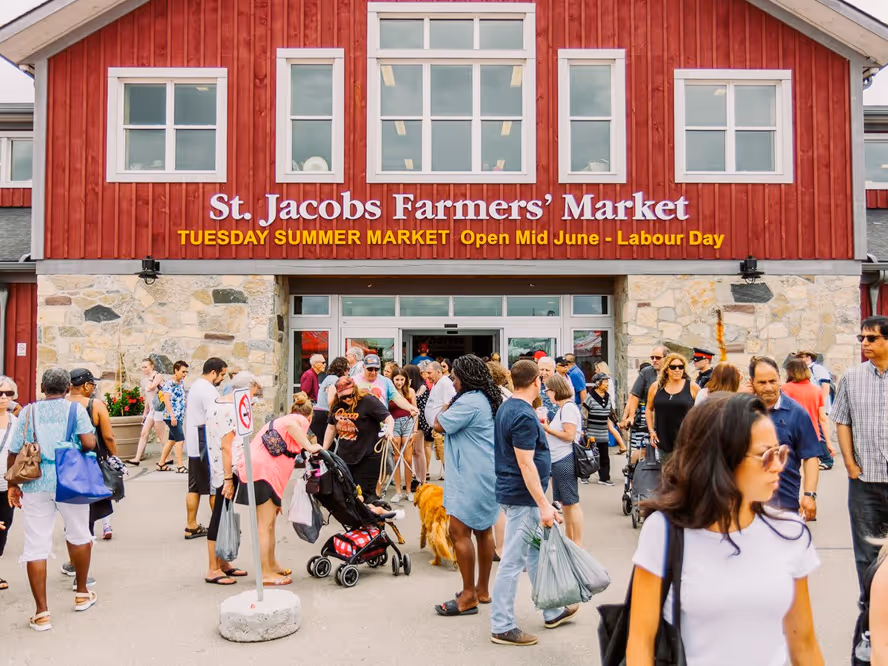 Crowd outside red building entrance of St. Jacobs Farmers' Market on a busy day.