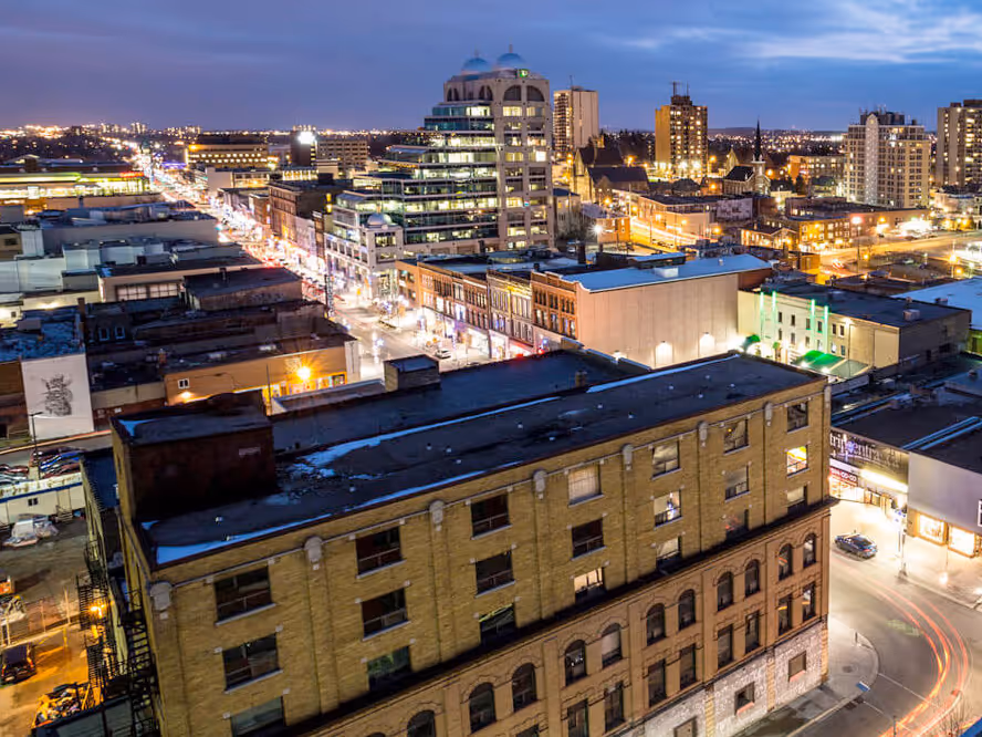 Evening cityscape with lit streets and buildings, including a prominent modern glass building.