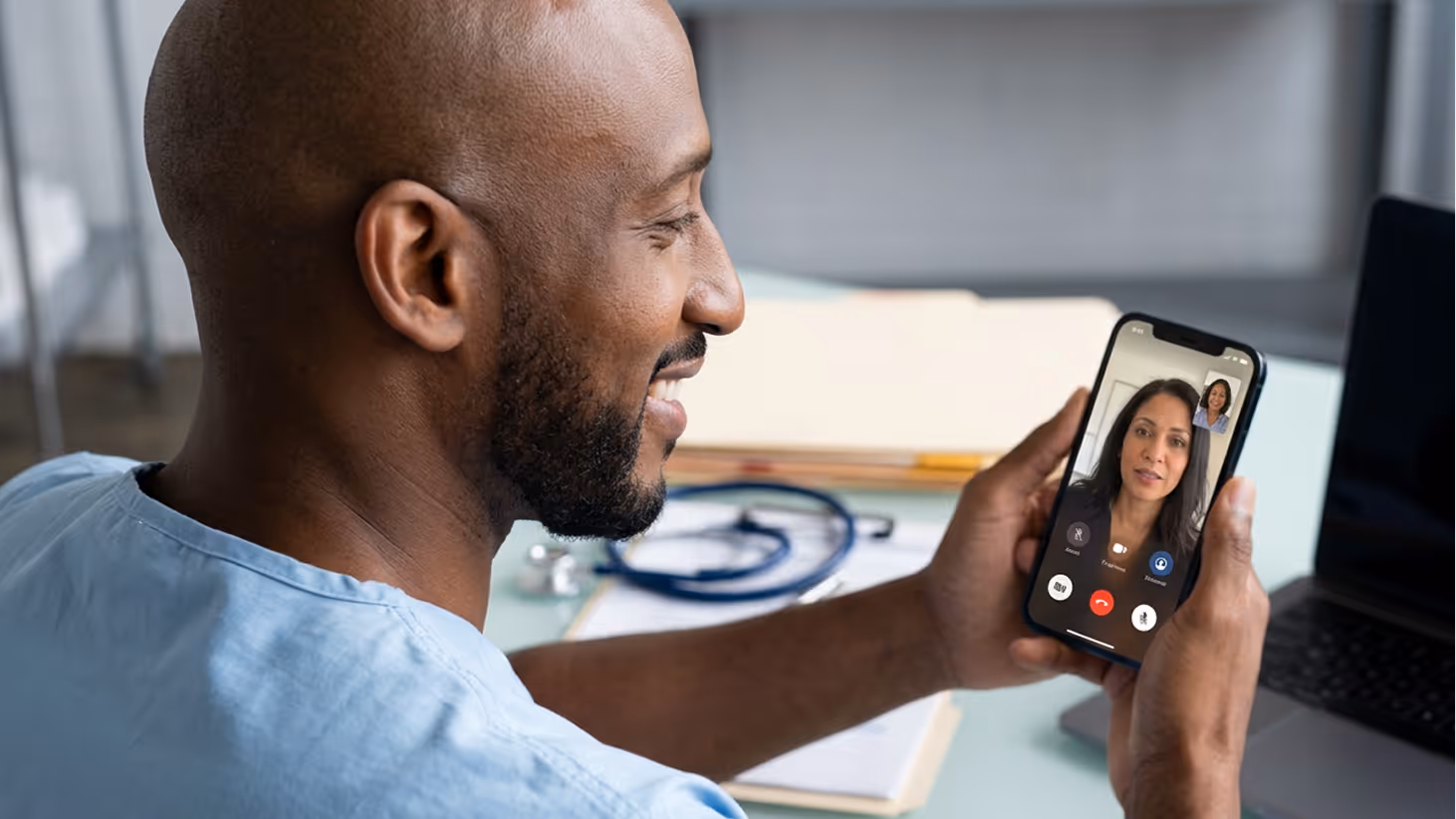 Man in medical scrubs smiling while having a video call with a woman on a smartphone.