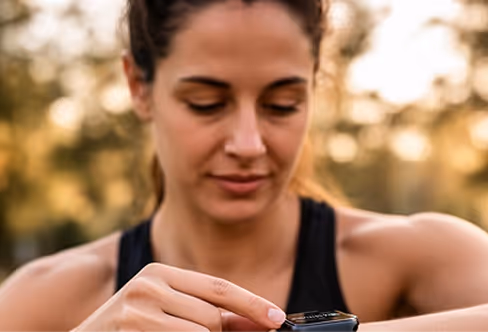 Woman outdoors checking her smartwatch on wrist, wearing a black tank top.