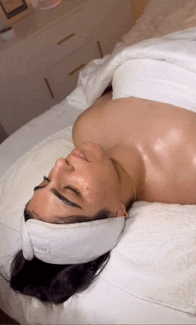 Woman with headband relaxing on spa bed receiving a facial massage treatment.