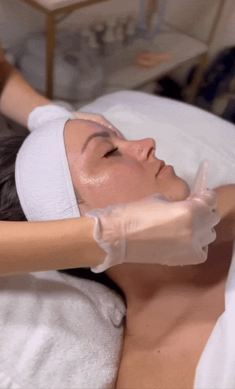 Woman receives gentle facial massage with gloves and headband in a spa setting.