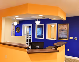 Reception desk area with orange walls, dark blue accent wall with framed pictures, and two pendant lights overhead.