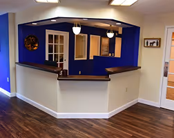 Reception desk area with dark blue accent wall, two hanging lights, and wood flooring.