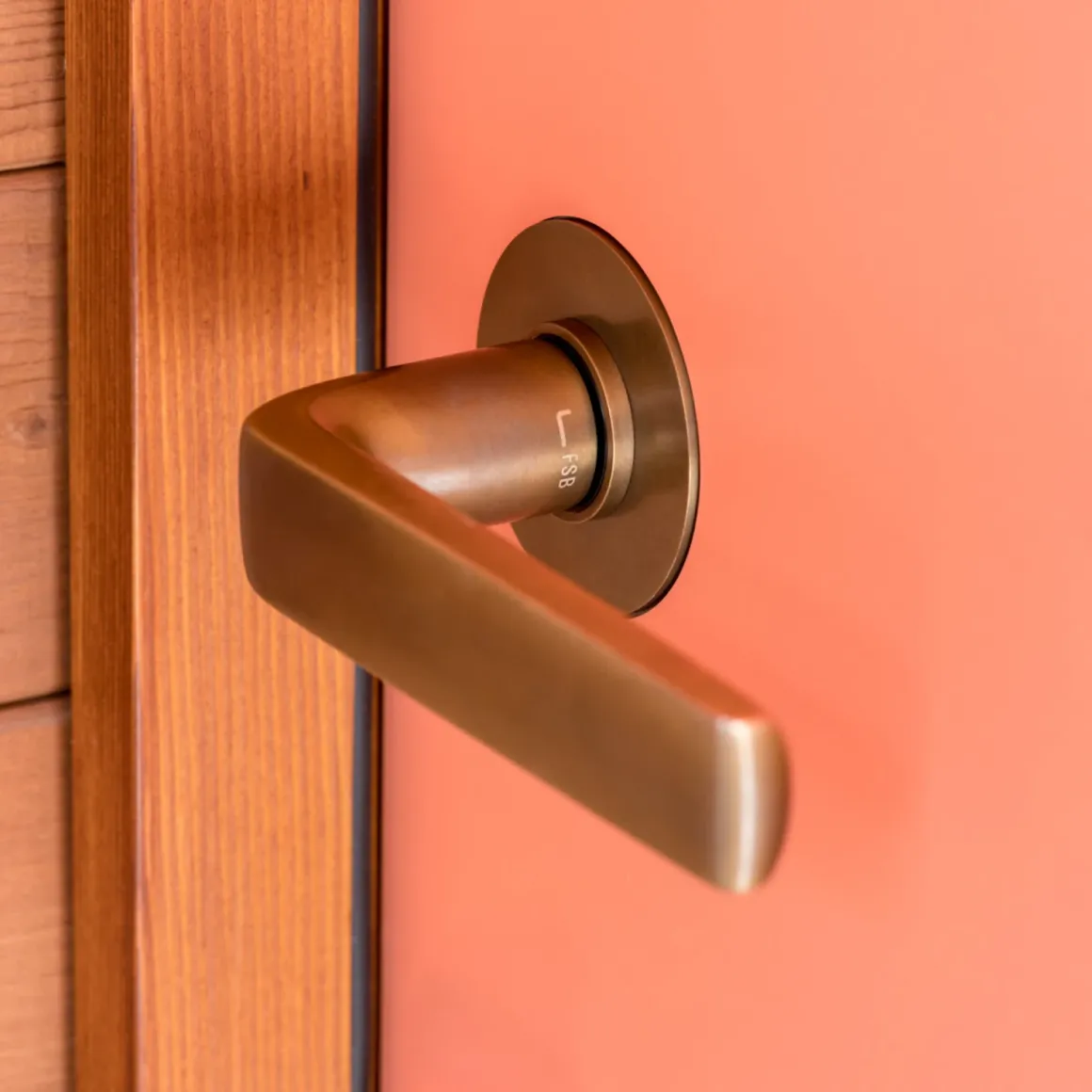 Close-up of a bronze door handle on an orange door with wooden frame.