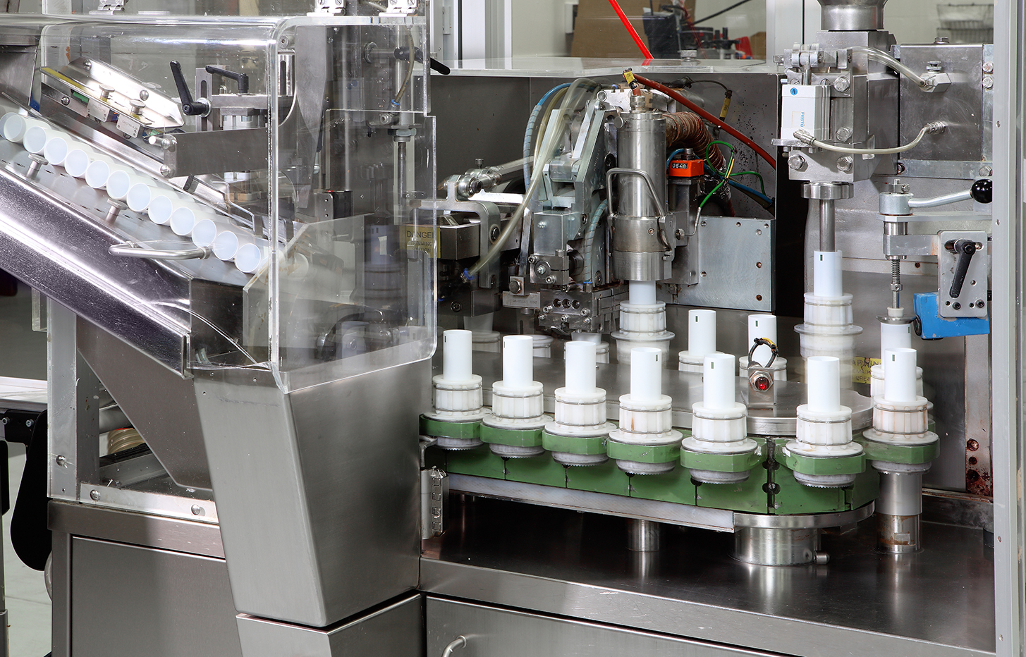 Industrial machine with white plastic components on a green rotating platform inside a stainless steel casing.