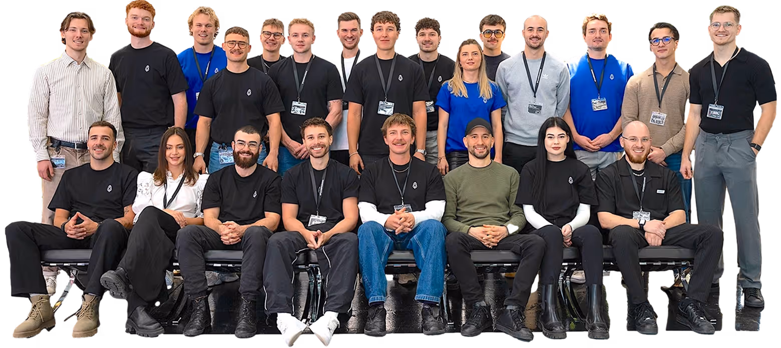 Gruppenfoto eines vielfältigen Teams aus Männern und Frauen, einige sitzen und einige stehen, die meisten tragen schwarze T-Shirts mit Firmenlogo und Namensschilder.