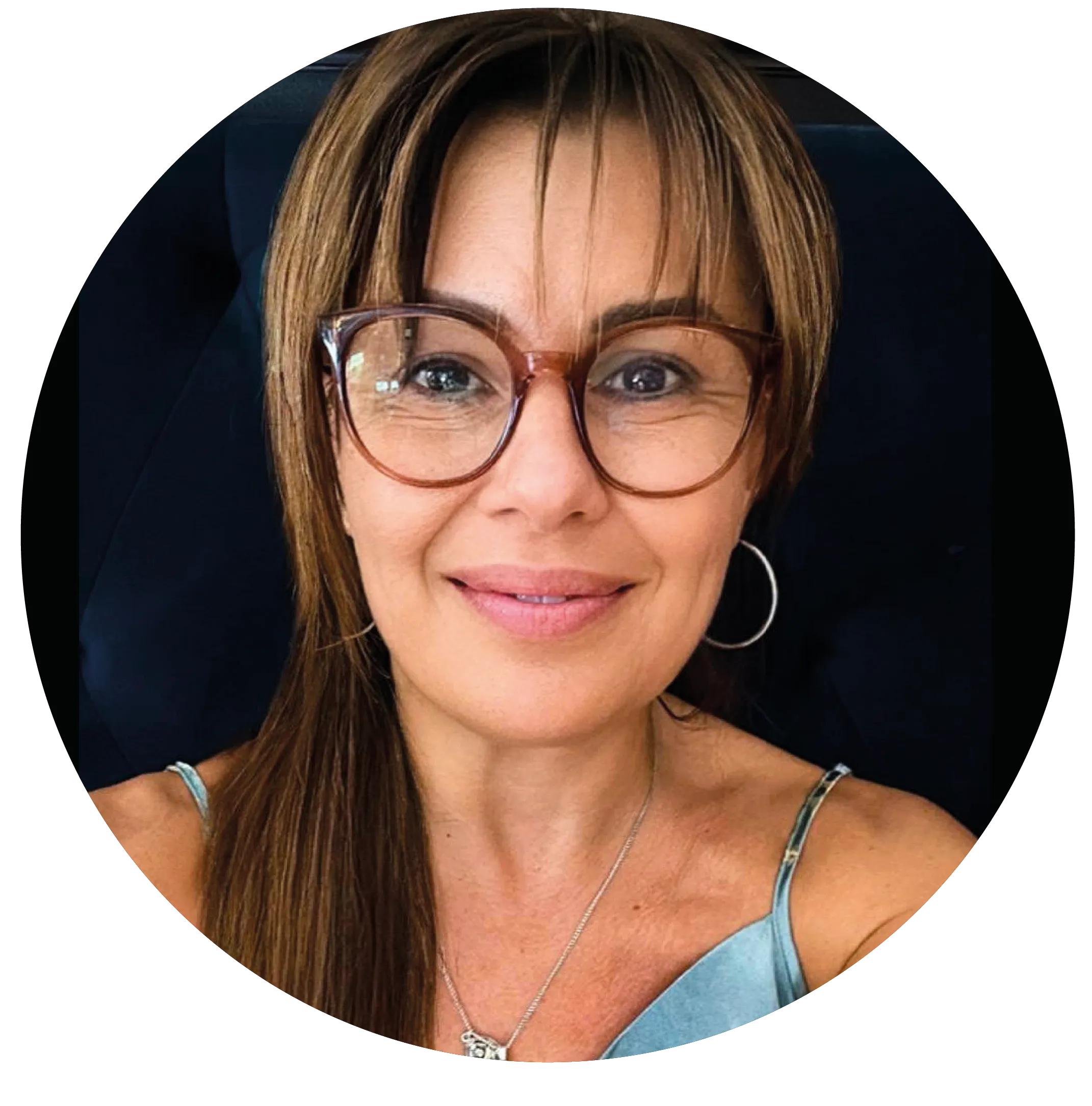 Mujer con gafas marrones y cabello castaño, sonriendo, con pendientes de aro y camiseta de tirantes celeste.