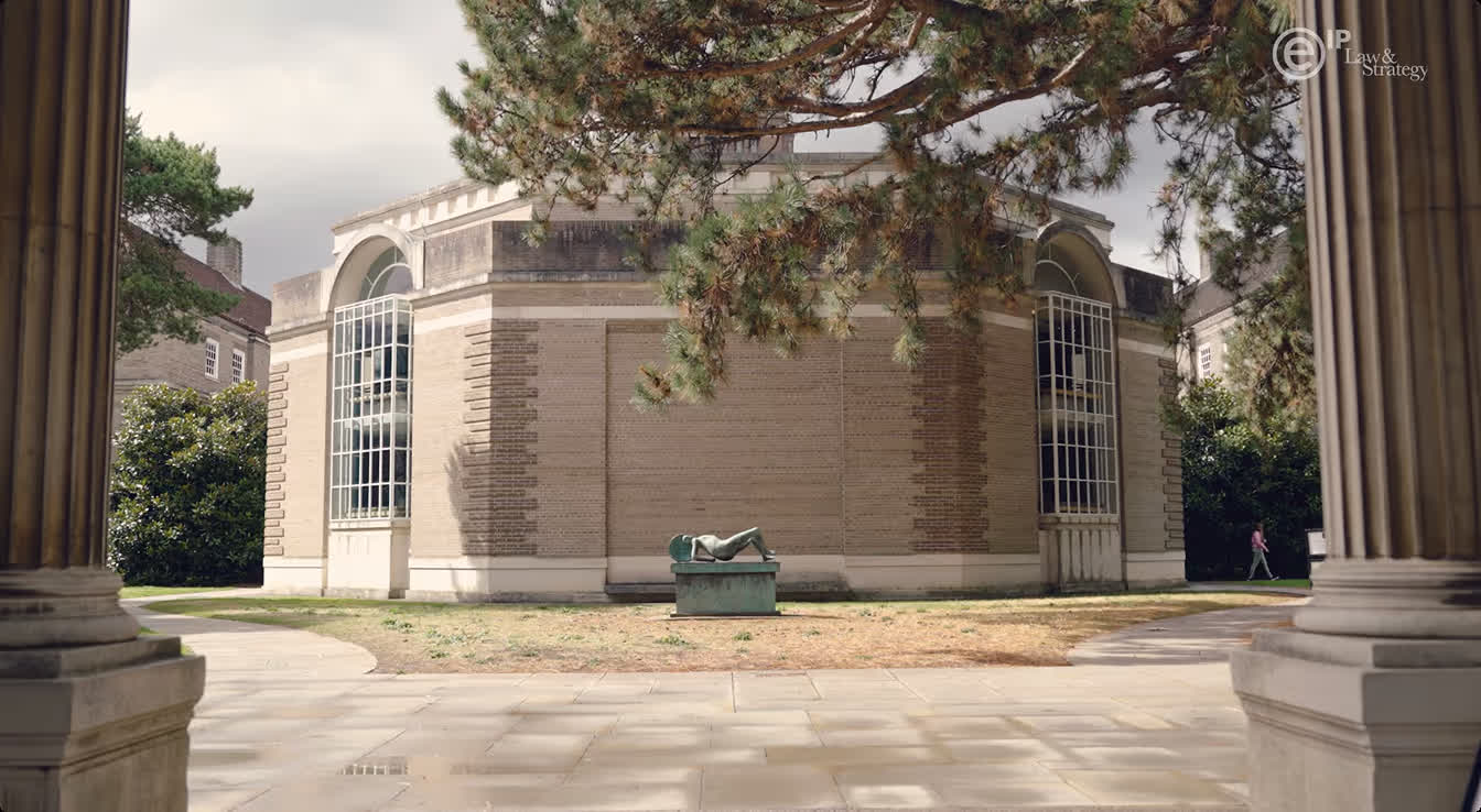 Stone building with large arched windows and a reclining statue in the center courtyard, framed by tree branches and columns.