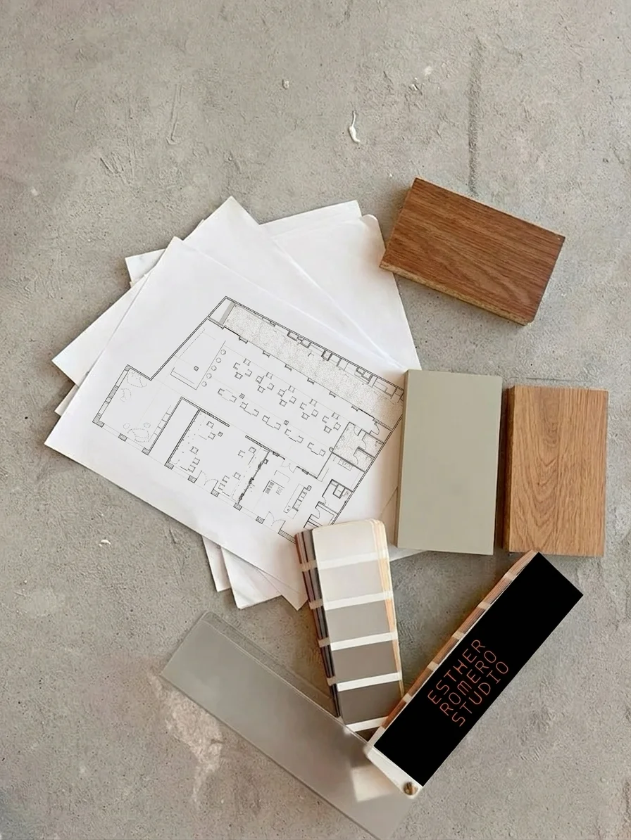 Planos arquitectónicos con muestras de maderas y paleta de colores sobre suelo de cemento.
