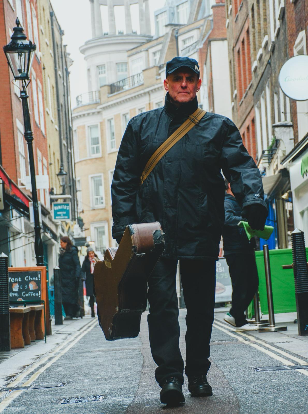 John Wroath walking with guitar case.