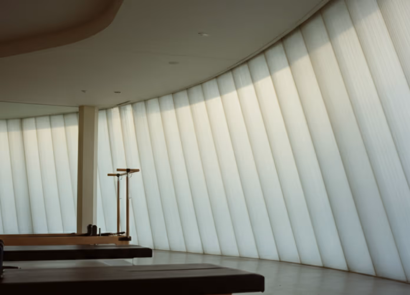 Sunlit pilates studio interior with reformer beds and curved fabric panel walls
