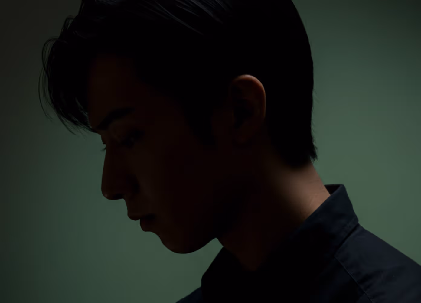 Profile portrait of a young person in soft shadow against a deep green background