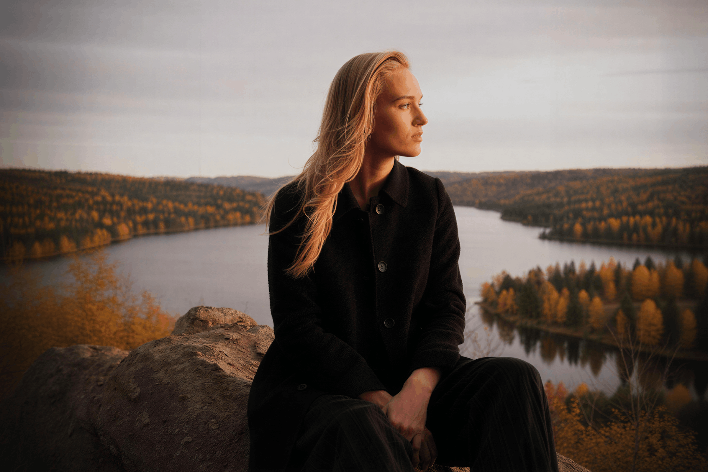 Woman sitting calmly on a rock above a lake in soft evening light