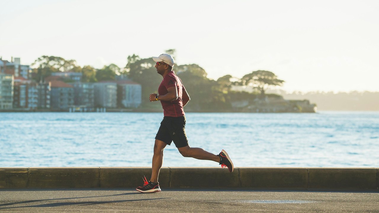 Man running along a waterfront promenade in morning light